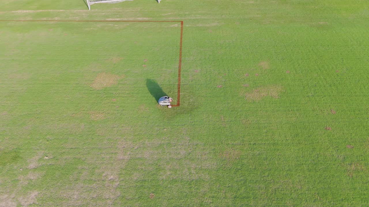 A robot autonomously paints precise lines on a soccer field. Aerial view captures its systematic movement and efficiency