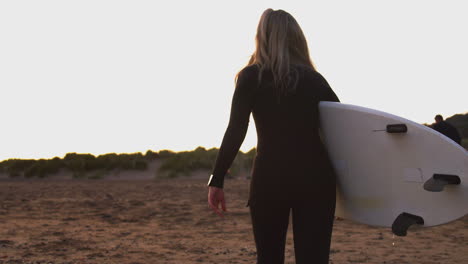 Rückansicht-Einer-Frau-Im-Neoprenanzug,-Die-Nach-Dem-Surfen-Ein-Surfbrett-Den-Strand-Hinauf-Trägt