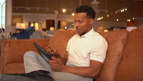 Enthusiastic-African-American-Man-Using-Tablet-on-Sofa-in-Furniture-Store