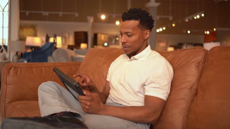 enthusiastic african american man using tablet on sofa in furniture store
