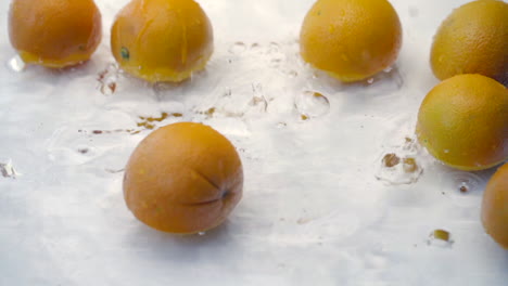 slomo of oranges falling into water on white backdrop