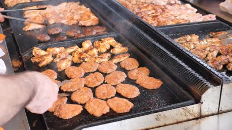 a cook grilling chicken and burgers on a hot griddle in the street