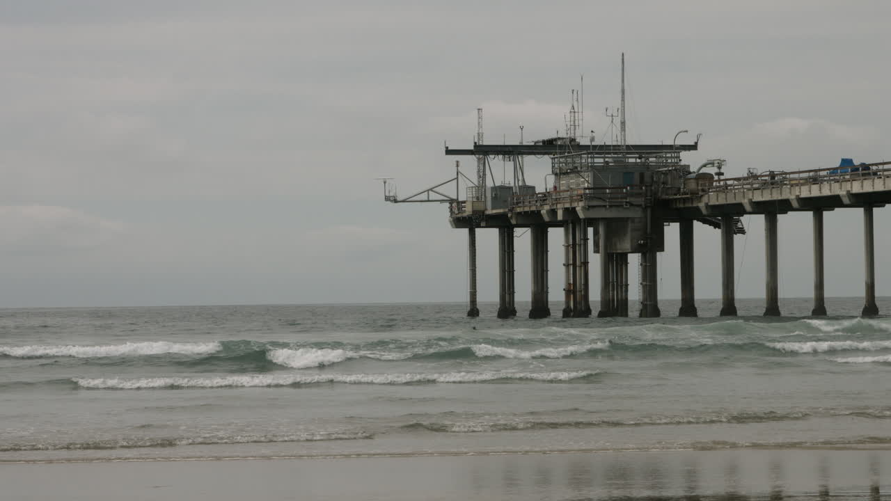 A tranquil overcast morning at Scripps Pier in La Jolla, with soft waves rolling ashore and the iconic pier stretching into the Pacific, capturing the serene beauty of Southern California’s coast
