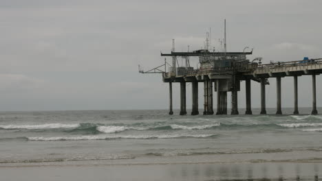a tranquil overcast morning at scripps pier in la jolla, with soft waves rolling ashore and the iconic pier stretching into the pacific, capturing the serene beauty of southern california’s coast
