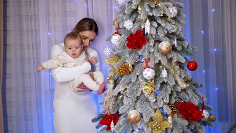 mother with her baby at the beautiful christmas tree. mom shows the festive décor to her child.