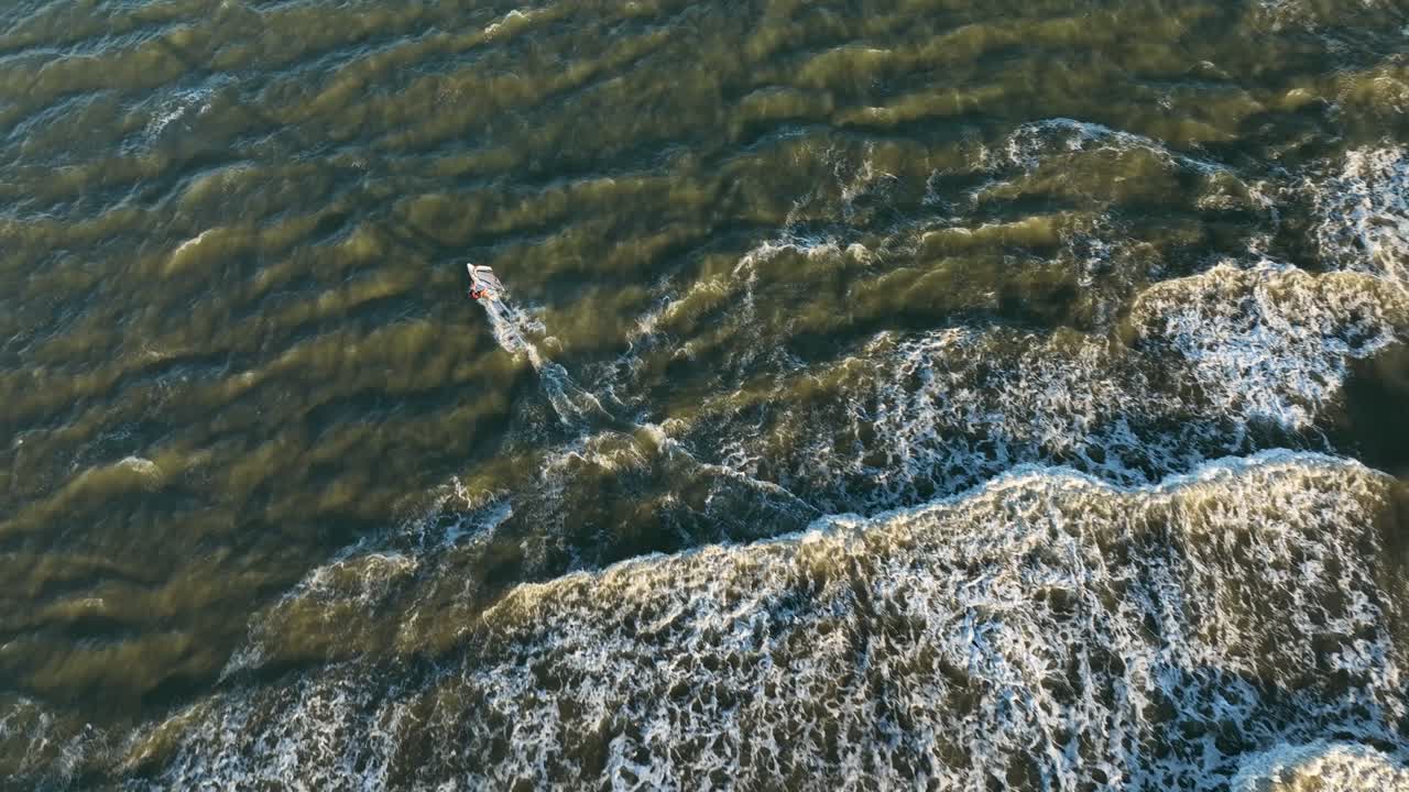 Windsurfer riding waves out to shore, overhead aerial view