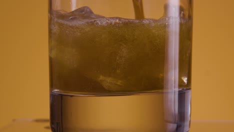 primer plano de un vaso vacío contra un fondo amarillo dorado con un ajuste de luz naranja en el que caen los cubitos de hielo y se llena con cola