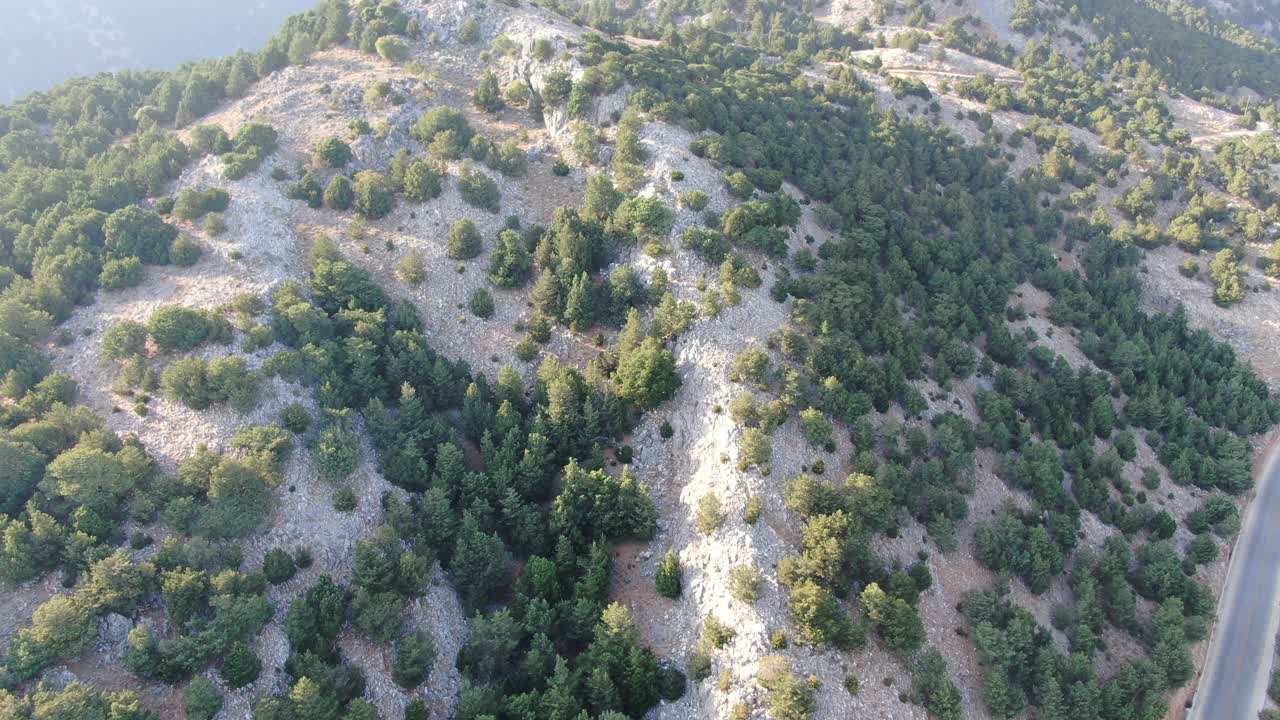 vista de avión no tripulado en grecia volando sobre una montaña marrón y verde con carretera de serpiente y mar en el horizonte en un día soleado