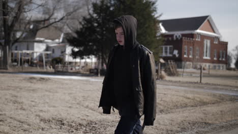 a young high school aged teen boy wearing a backpack walking down a road during the winter on a cold day-2