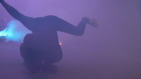 slow motion shot of african youth doing impressive bread dancing spins on his back in colorful smoke