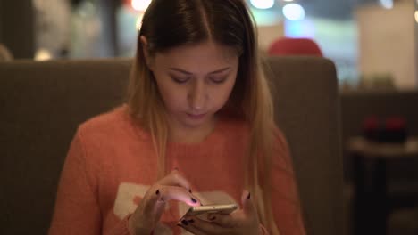 una joven hermosa se sienta en un café y trabaja en un teléfono inteligente