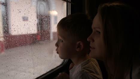 madre y hijo en el tren mirando por la ventana en un día de lluvia