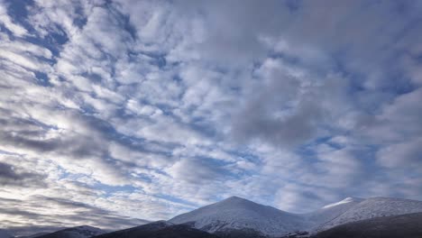 observe la cautivadora transformación del cielo mientras las nubes se desplazan con gracia sobre majestuosas montañas cubiertas de nieve durante un tranquilo día de invierno