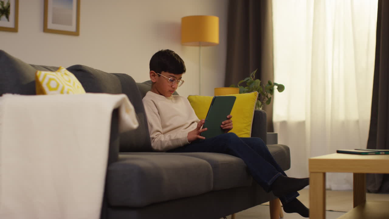 Young Boy Goes To Sit On Sofa At Home And Play Games Or Stream Content Onto Digital Tablet 2