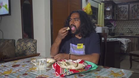 a long-haired indian man having a bite of his traditional meal at his home's dining room table