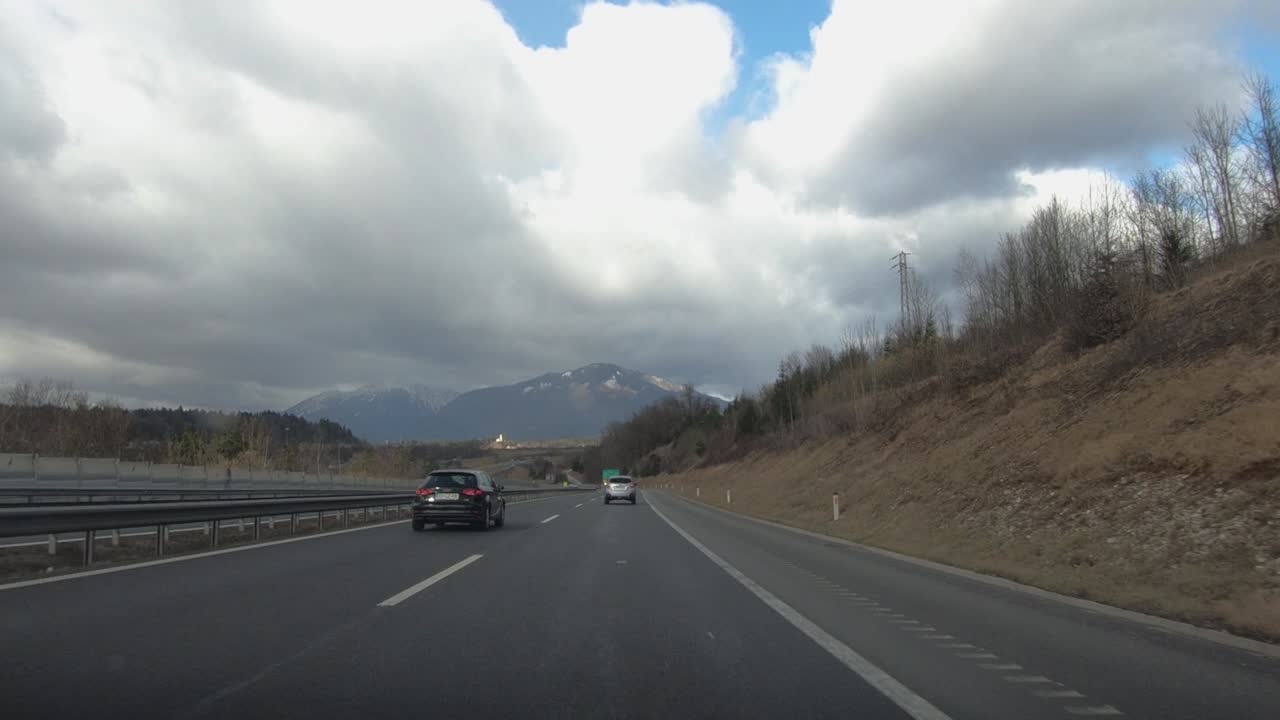 Driving on a scenic highway with mountains and cloudy skies, passing road signs