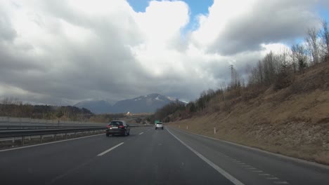 driving on a scenic highway with mountains and cloudy skies, passing road signs