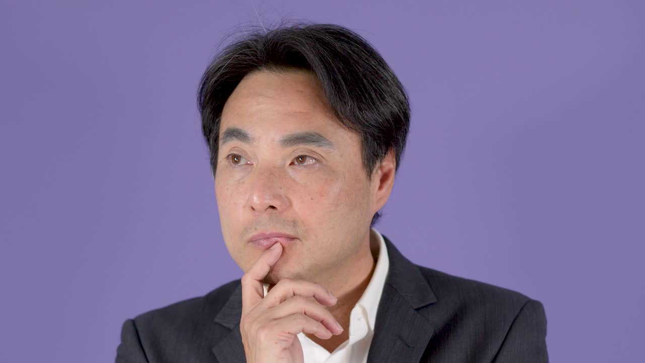 考え事をしているスーツ姿の中年ビジネスマン、わずかな頭の動き、固定カメラ、ソフトなスタジオ照明。