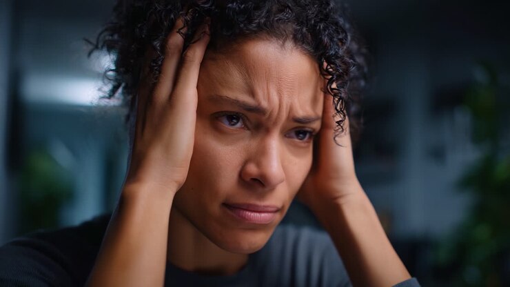 Eine Frau zeigt tiefe emotionale Not und Angst, hält sich frustriert den Kopf, während sie in einer schwach beleuchteten Umgebung überwältigende Gefühle und Herausforderungen erlebt