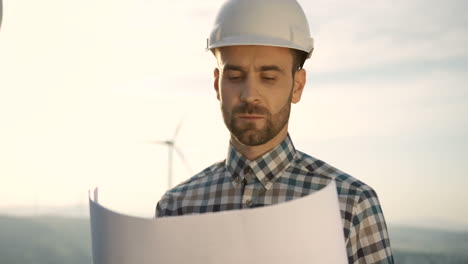 vista de cerca del ingeniero caucásico con casco y viendo algunos planos en la estación eólica de energía renovable