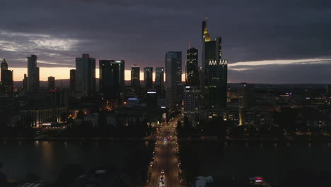 AERIAL:-Wide-Establishing-Shot-of-Frankfurt-am-Main,-Germany-Skyline-at-Night-over-Main-River-and-Bridge-with-Little-Car-traffic