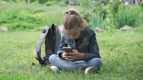 a nine-year-old girl sits in a park on the grass and types a text message on her smartphone. she uses a smartphone to browse social networks.
