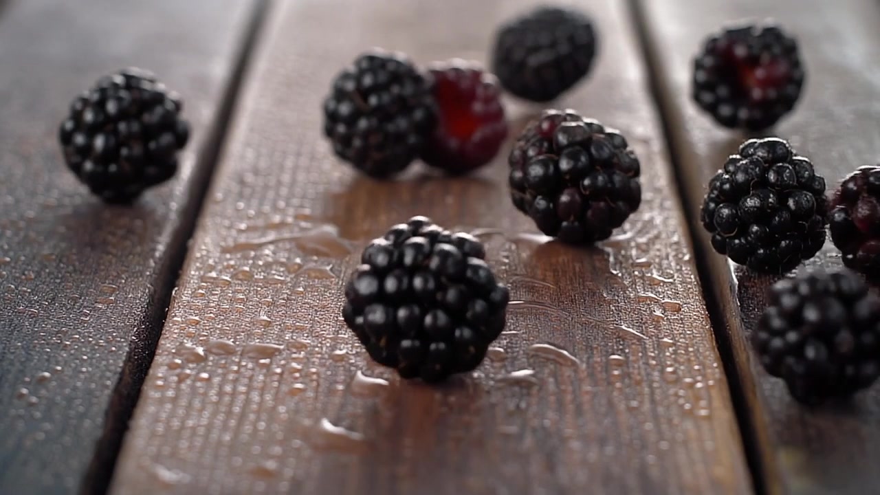 Moras frescas cayendo sobre una superficie de madera mojada.