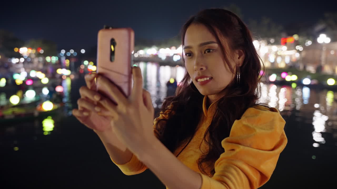 Bella donna asiatica scatta un selfie notturno accanto al riflesso del fiume a Hoi An, Vietnam.