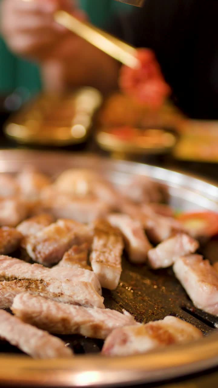 Gambar vertikal daging yang dipanggang di atas hotplate dengan sumpit mencelupkan makanan ke dalam saus