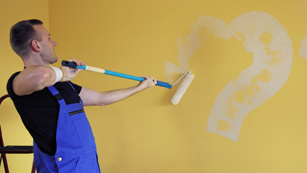 Man painting heart on a wall during makeover in flat. Painter improving the wall of a room with the roller on a long handle. Home repair.