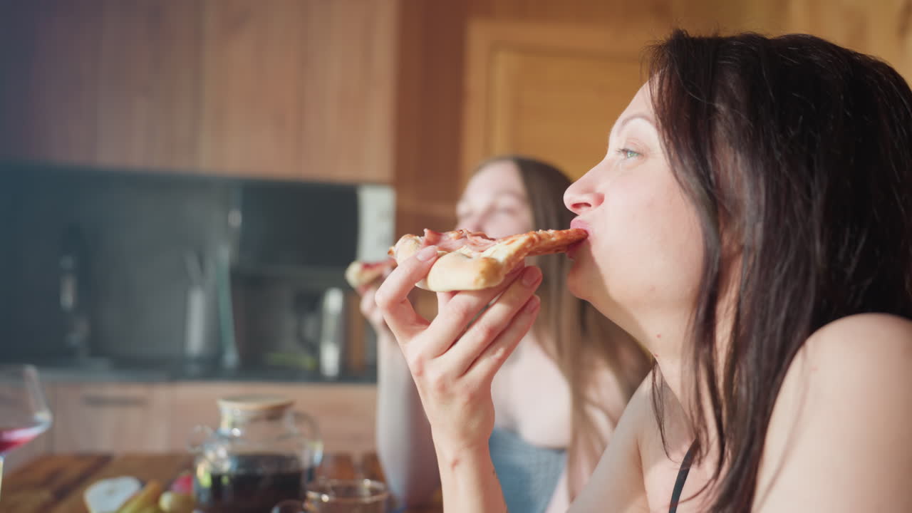 Two students having a good time as they enjoy a slice of pizza, sharing a relaxed moment in the kitchen, laughing and savoring their meal with joy