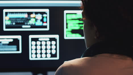 Rear-View-Of-Female-Teenage-Hacker-Sitting-In-Front-Of-Computer-Screens-Bypassing-Cyber-Security