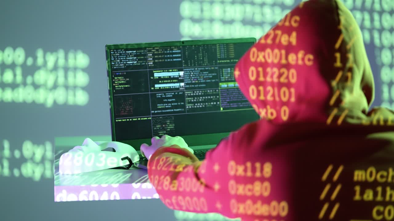 A masked individual in a hoodie types on a laptop while hexadecimal digits and system code illuminate their workspace. A white mask lies nearby, representing anonymity in the digital shadows