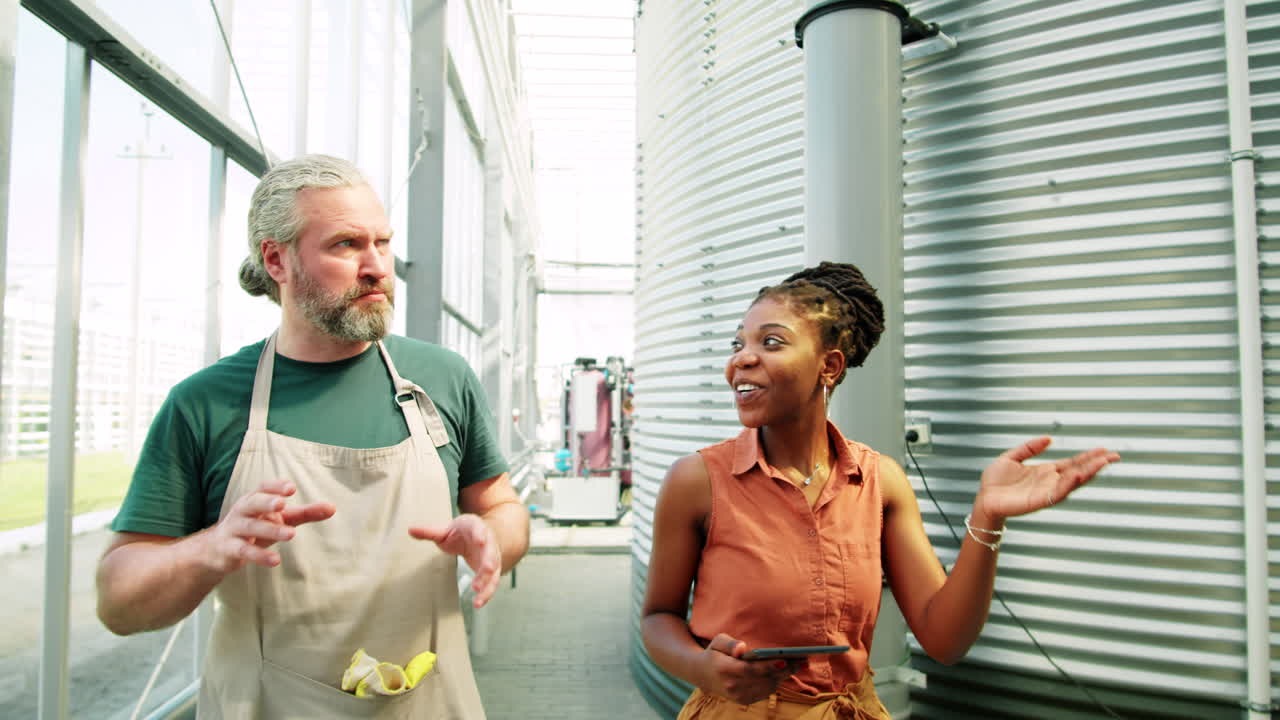 Coworkers Walking with Tablet and Discussing Water Tank in Greenhouse