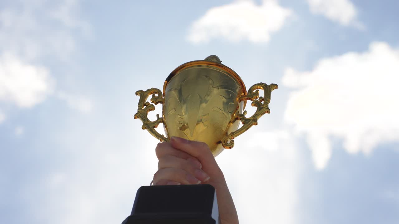 Hand holding award trophy outdoors with sky background. Concept of achievement, success, victory, recognition, and motivation. Symbol of accomplishment and celebration