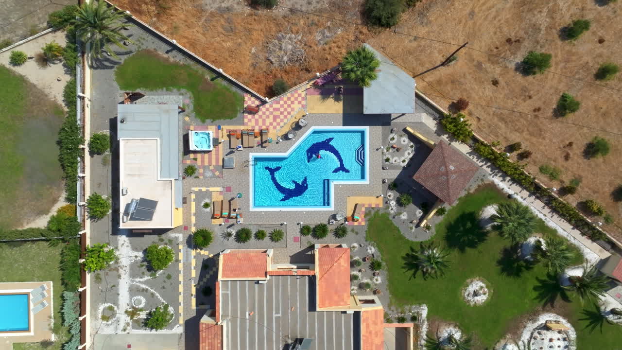 Top down drone shot of a woman swimming in a pool, at a villa in sunny Greece