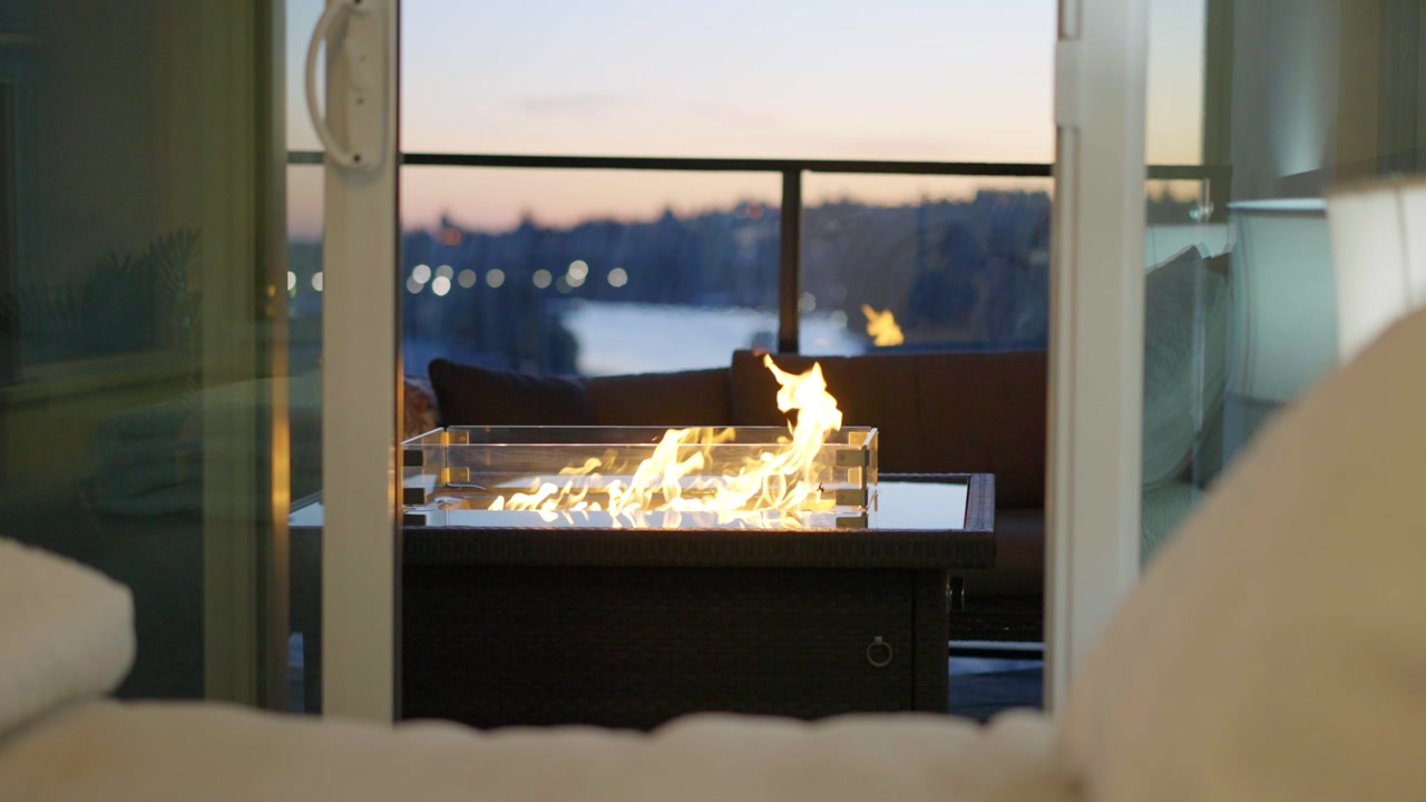 Close-up view of a modern fire table on a high-rise balcony at dusk, creating a warm and relaxing atmosphere with soft city lights beyond.