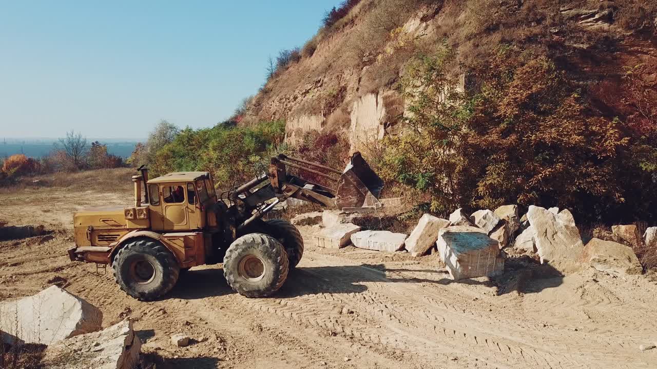 professional yellow bulldozer is working near sand quarry on the background of stones. Camera motion straight