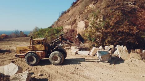 professional yellow bulldozer is working near sand quarry on the background of stones. camera motion straight