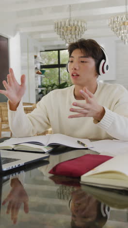 vertical video of asian male teenager using laptop in living room
