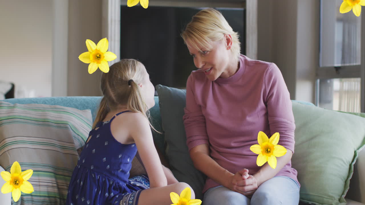 Animation von Blumen über kaukasischer Mutter und Tochter, die auf dem Sofa sprechen und lächeln