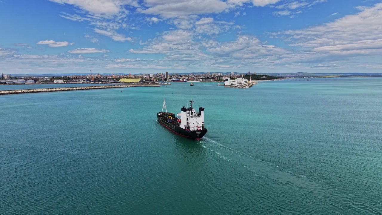 Lastfartyg rör sig genom vattnet nära en stadshamn under dagen.