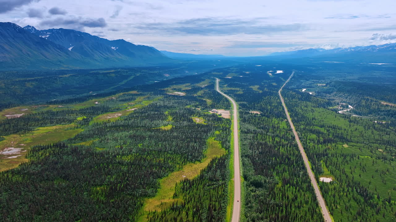 Two parallel roads crossing the huge green valley among the mountains. Hazy rocks surround the scenery. Alaska, USA. Aerial view