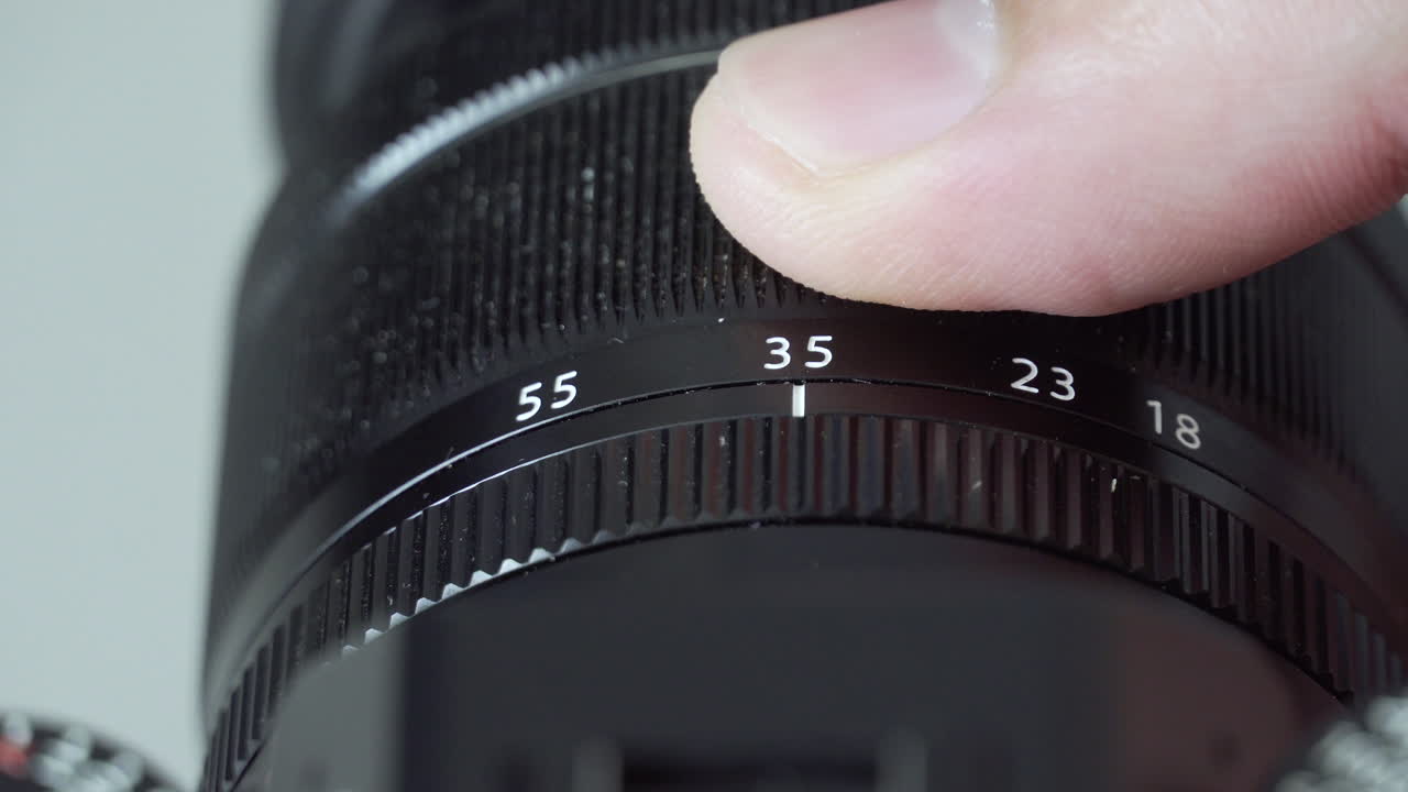 Male fingers adjusting zoom on black digital mirrorless camera lens close up