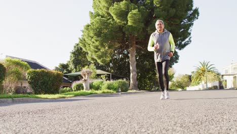 video of smiling senior biracial man in sports clothes running on sunny street