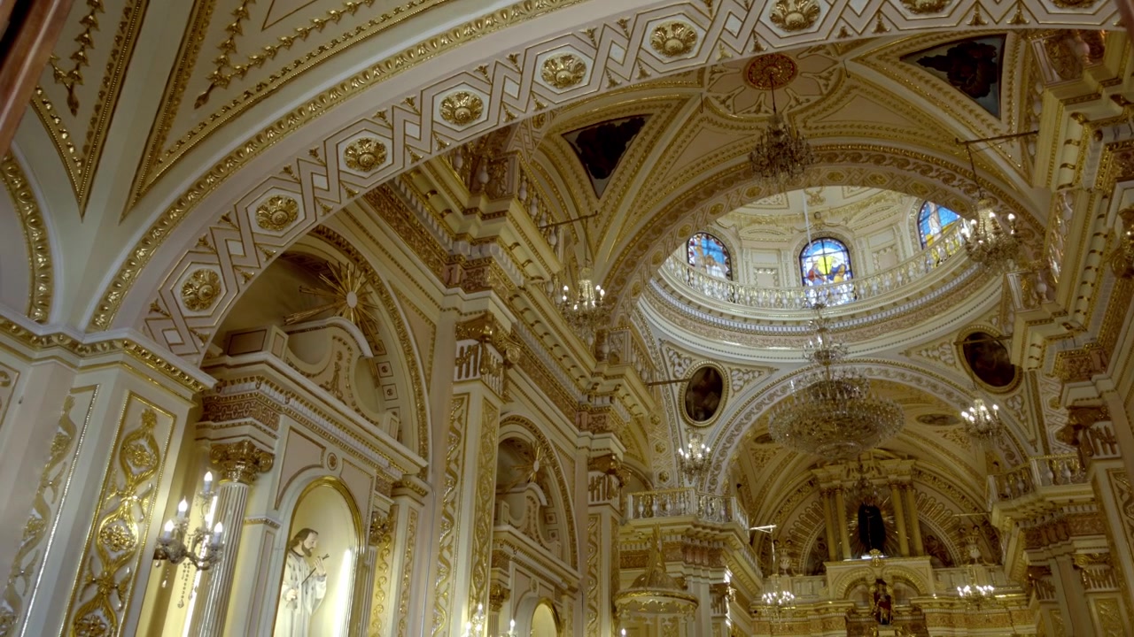 Vue de l'intérieur d'une église ornée avec un plafond détaillé, des lustres et des arches, une décoration riche et une symétrie, une architecture religieuse historique à Cholula Puebla capturée sous une lumière douce.