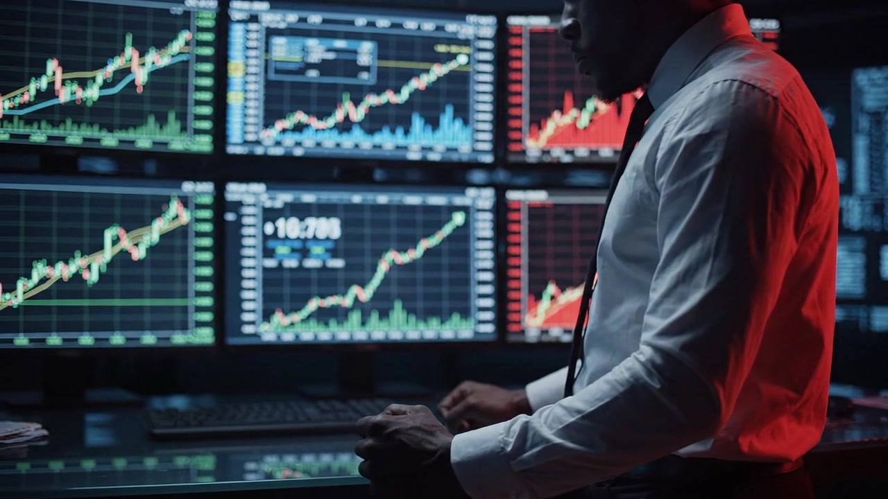 Trader uomo concentrato che analizza dati del mercato azionario su più monitor con grafici vivaci indicativi di tendenze di mercato e fluttuazioni dei prezzi