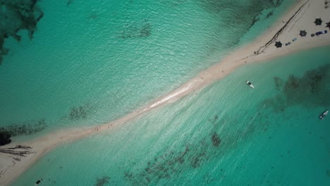 A-sandbar-in-turquoise-ocean-waters,-people-and-boats-visible,-bright-day,-aerial-view