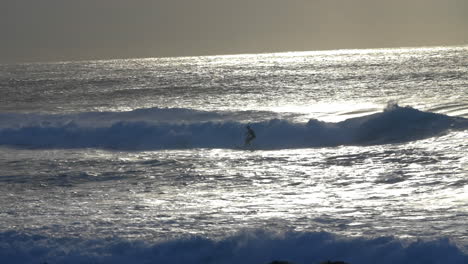 silhouette of surfer surfing in ocean at sunrise from bronte beach in sydney, nsw, australia