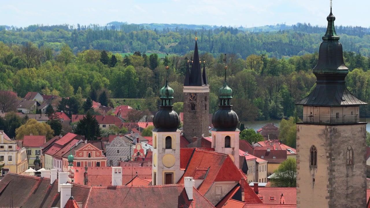 Vista aérea de alta altitude de uma cidade histórica checa com uma colorida praça renascentista, castelo e lagos gêmeos, rodeada por campos verdes ondulantes e colinas arborizadas, Telč, República Checa